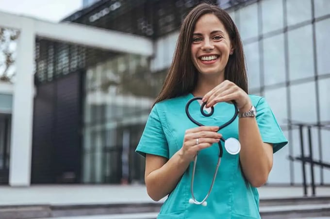 Pflegekraft mit Stethoskop vor einem Klinikgebäude