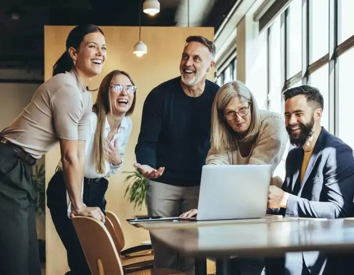consultingheads, agentur, viele menschen am Tisch, schauen auf laptop, lachen und unterhalten sich